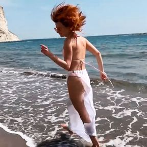 Sexy red-haired girl enjoys a walk by the sea