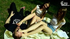 Two barefoot girls in a park have their feet worshiped by a stranger