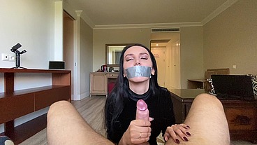 A sexy brunette with a taped-up mouth is passionately jerking off a big cock