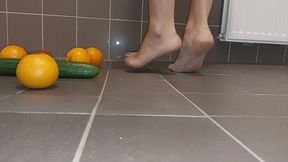 Sandra is crushing a lot of different fruits barefoot: Cucumbers, oranges, tomatoes, banana's