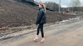 A girl in transparent high-heeled boots with exposed toes walks through deep mud