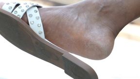 Beautyful feet soles with slippers in crossed legs, foot fetish close-up details, admiration.