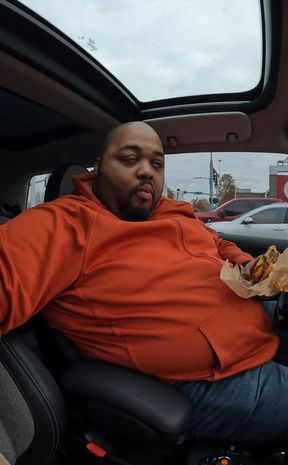 Fat guy in a small car eating McDonalds.