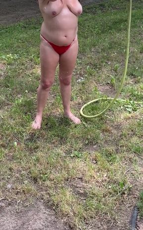 Naked woman holding hose in backyard