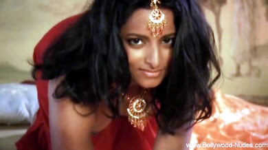 Dark-haired Indian mistress glows in red silk and gold under warm candlelight