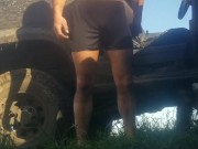 Grown man pees himself in shorts and bare feet outdoors in the grass by the dirty truck