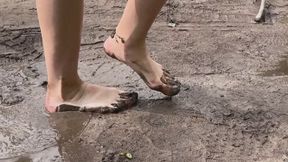A girl walks barefoot through deep slimy mud and gets her heels and toes dirty