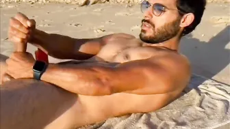 Muscular tattooed guy jerks his big cock on a nude beach
