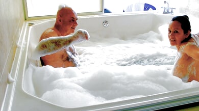 Slovakian woman and older man share a foamy nude bath in sunlit bathroom