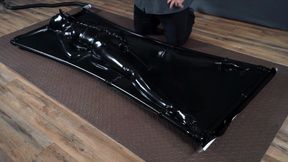 Tied up inside a black latex vacuum bed with an inflatable gag and vibrator