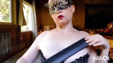 Strict dominatrix in black corset and mask disciplines with paddle and flogger