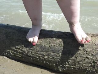 Bulky nude legs with red pedicure walk along the bank of the river, fetish.