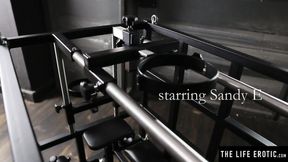 ”Kinky blonde Sandy E fingers her beaver in a BDSM cage”