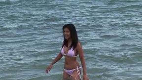 Happy smiling Asian brunette swims in the ocean and poses in her bikini