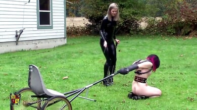 Blonde dominatrix leads bound submissive on leash through autumn forest