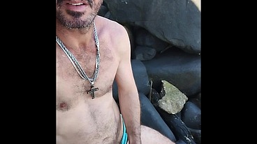 Esperando um puto para deixar ele duro nas pedras de uma praia de nudismo.