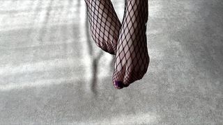 Girl in black fishnet pantyhose caresses her legs
