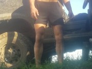 Grown man pees himself in shorts and bare feet outdoors in the grass by the dirty truck