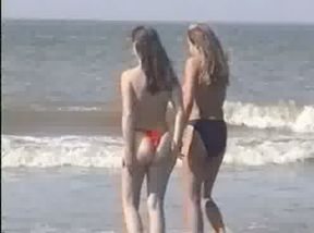 Two young blonde chicks walking on the sandy beach topless