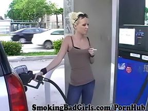 Cute blonde smoking cigarette at gas pump