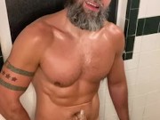 Muscular bearded man pisses in showet