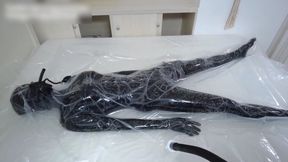 A girl bound in a leather bodysuit is confined inside a vacuum bag.