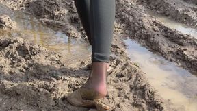 A girl walks through the woods in high-heeled sandals and steps on mud, loses her shoes, slips