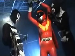 Sexy Super Hero in orange latex is strung up and tortured b